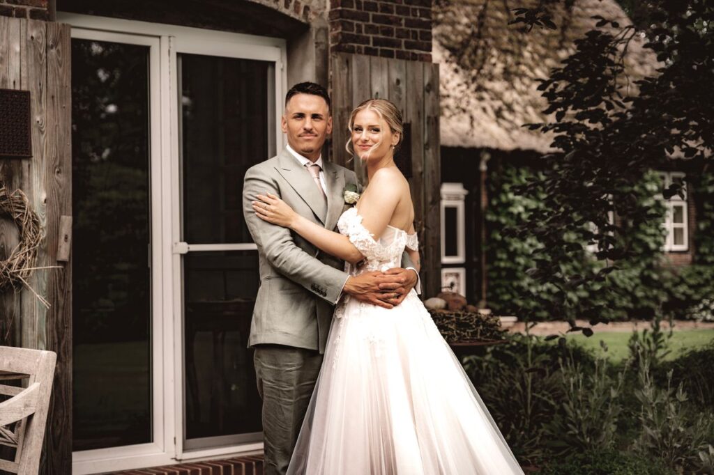 Bride and groom embrace outdoors in a charming rustic setting, capturing wedding day bliss.